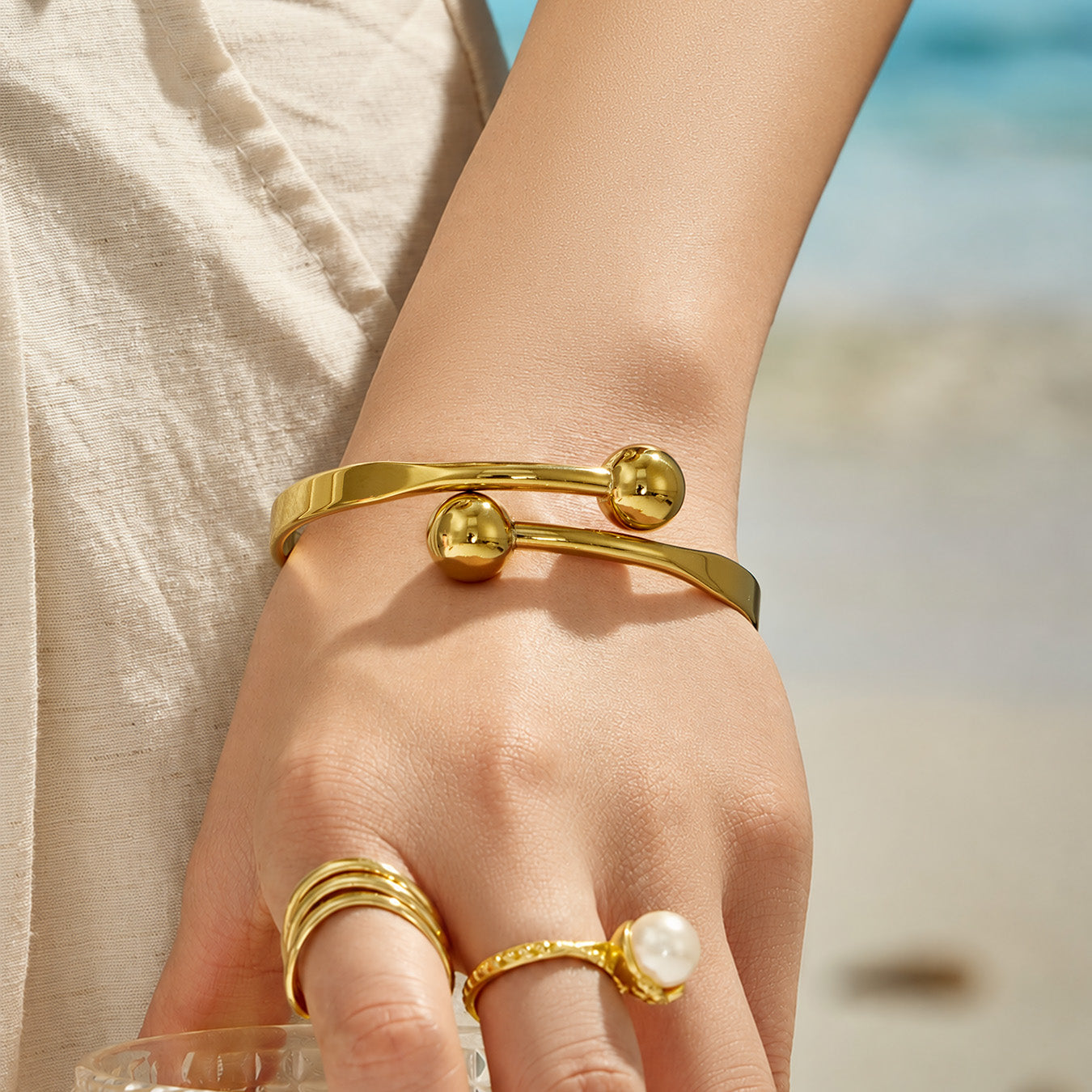 Gold double ball cuff bracelet styled with minimalist gold rings on a model hand