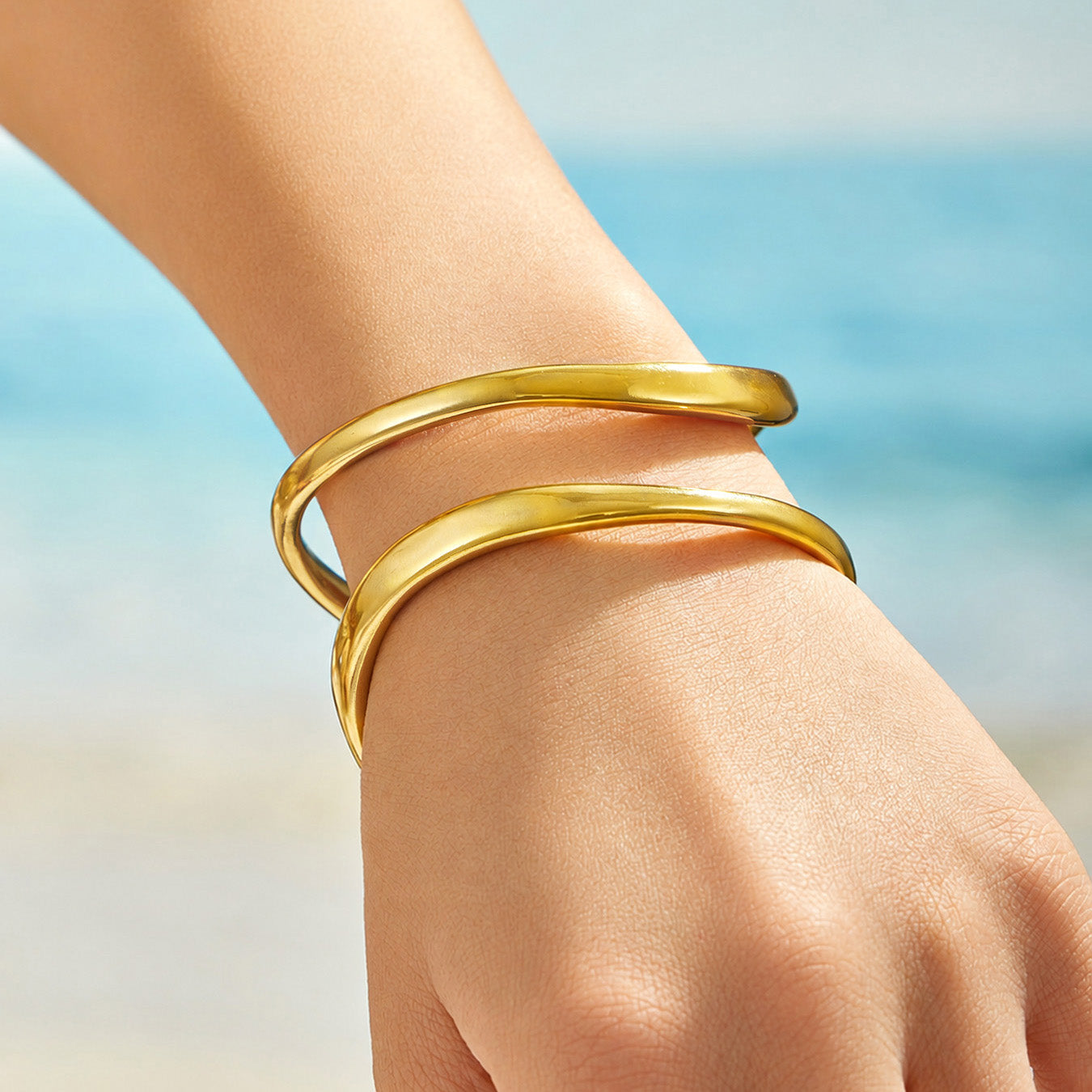 Gold double-band cuff bracelet shown on a model hand in an outdoor setting