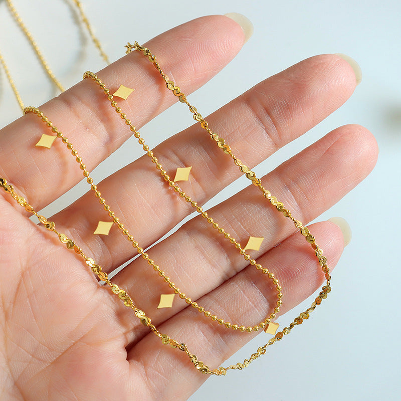 Close-up detail of a gold-tone double-layer geometric charm necklace shown in hand