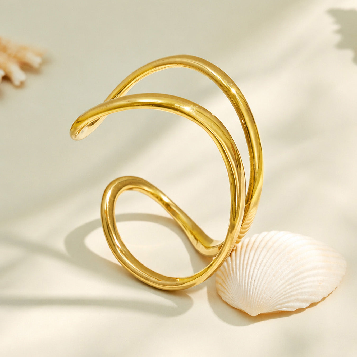 Gold double loop cuff bracelet displayed in a curved flat lay on a neutral surface