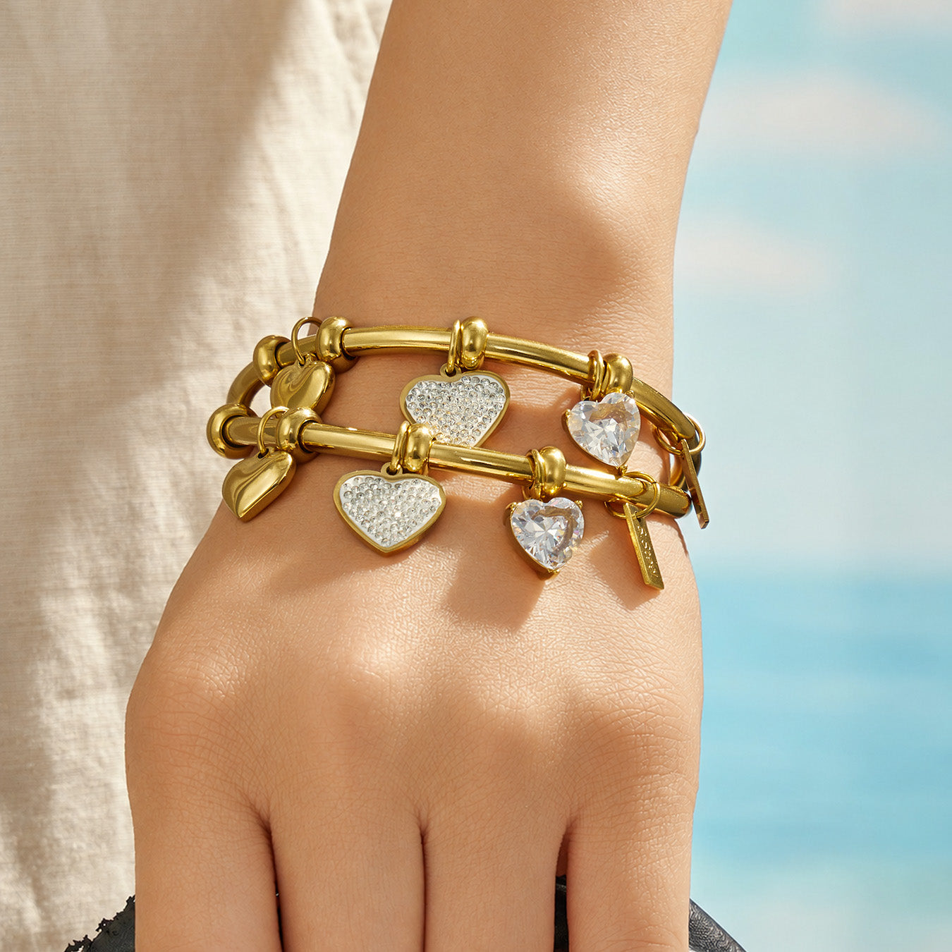 Gold heart bangle bracelet stacked with other bracelets on a model wrist