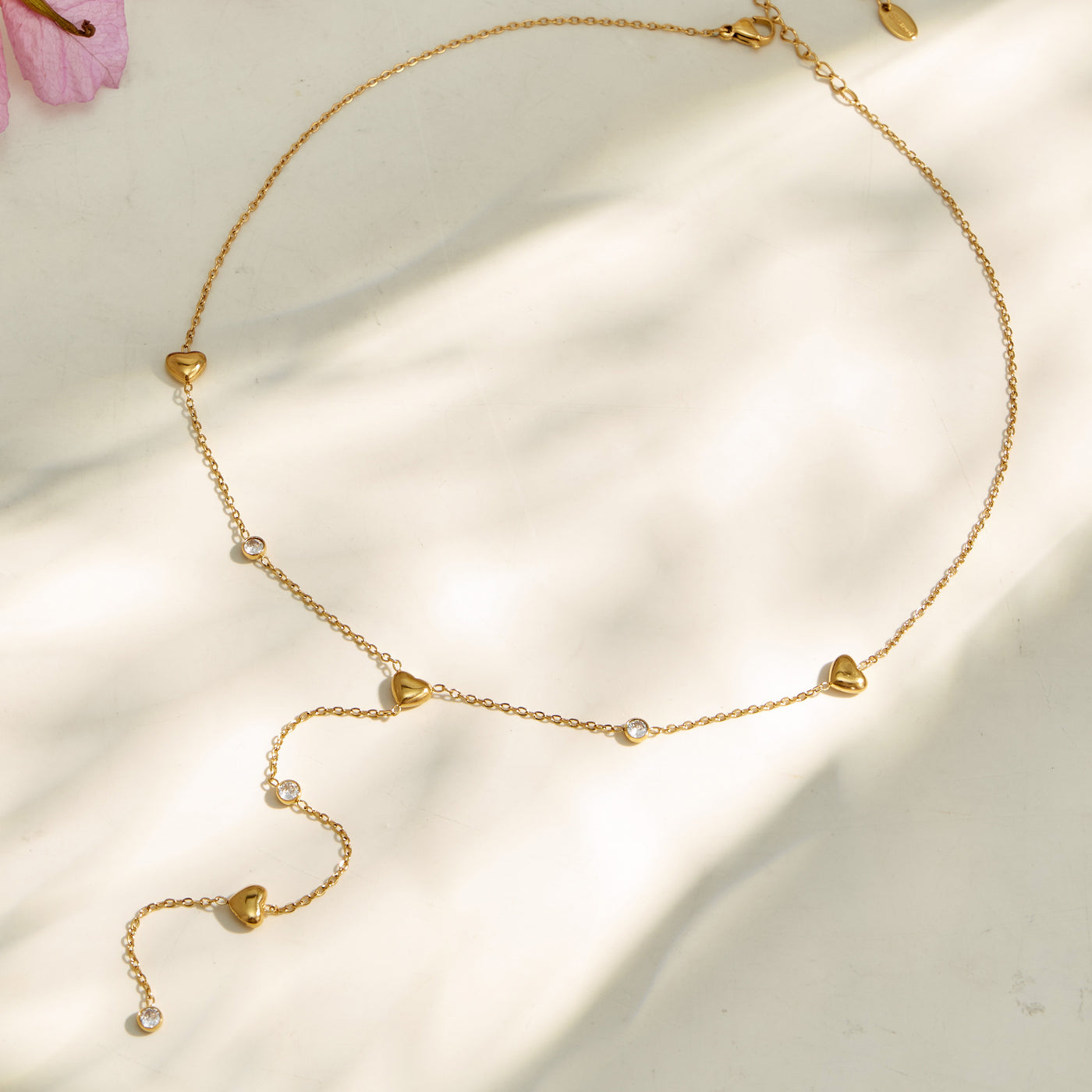 Gold heart lariat necklace arranged on soft neutral fabric with a long curved chain drop