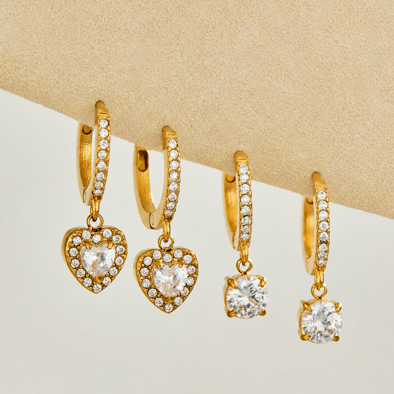 Gold heart and round CZ charm huggie earrings displayed on a neutral background