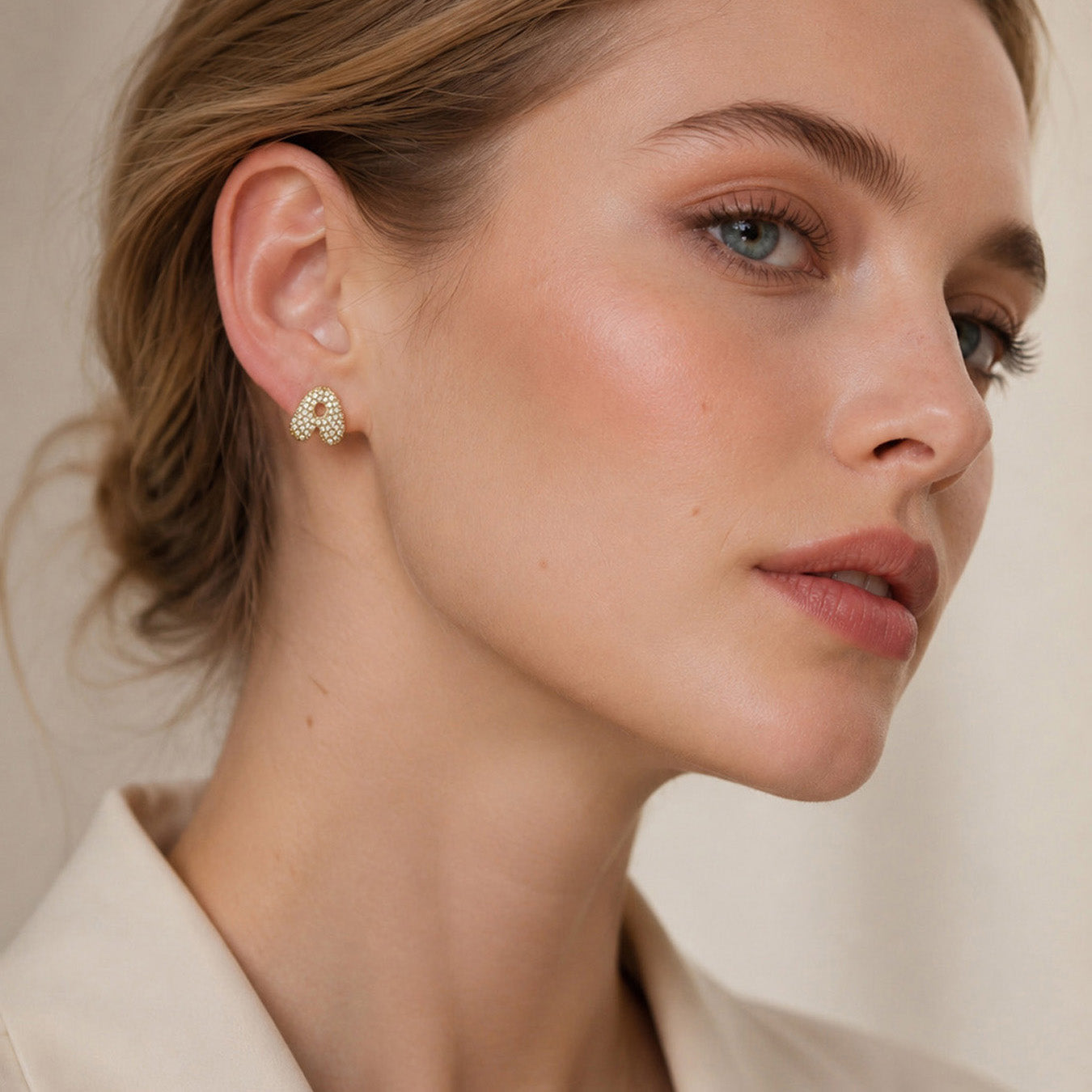 Model wearing gold alphabet stud earrings in a three-quarter view