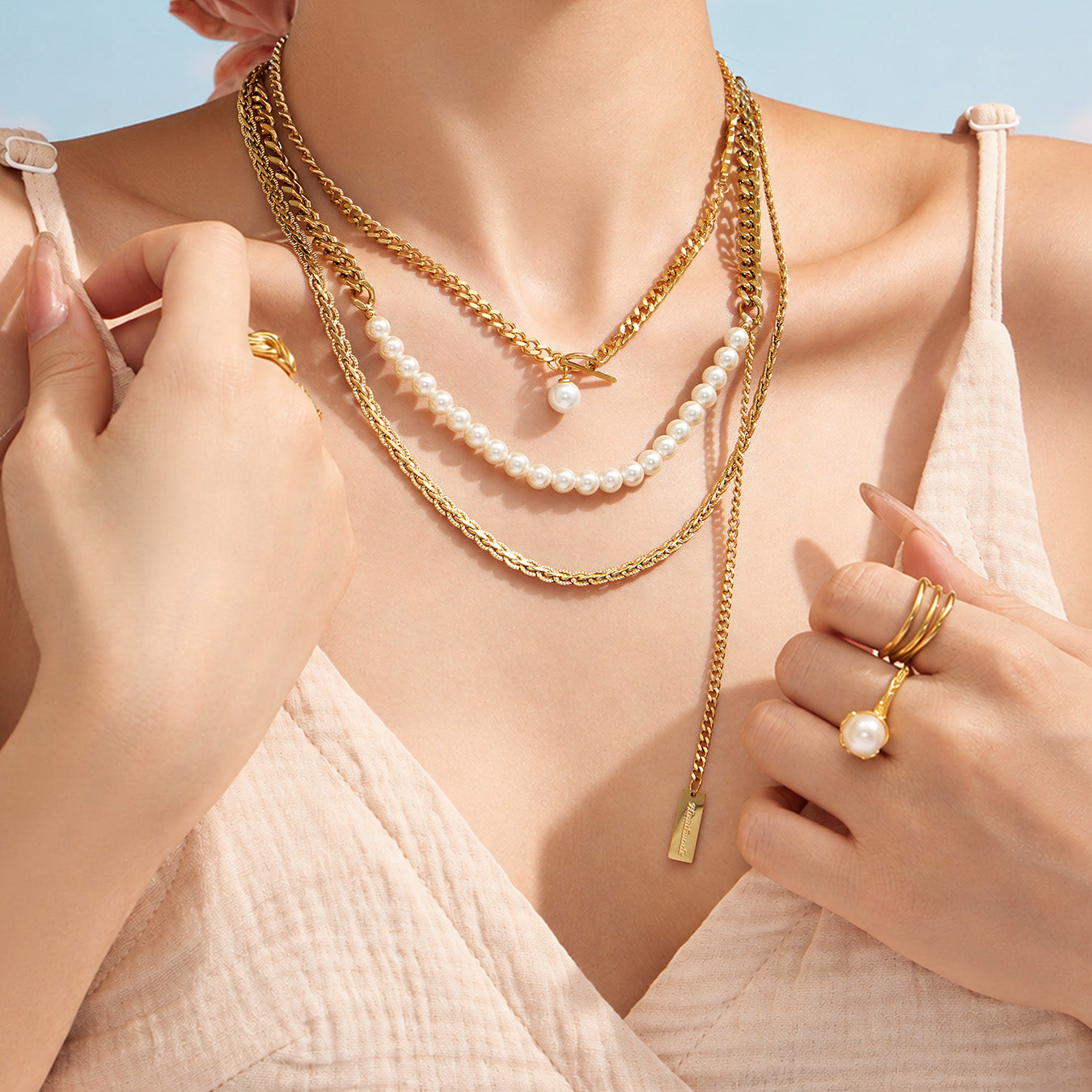 Model touching layered gold necklaces with faux pearl and minimalist chain details