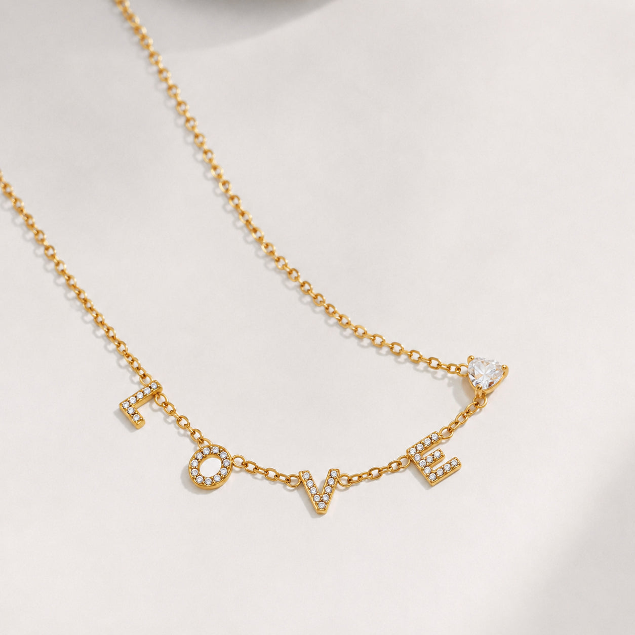 Gold LOVE letter zircon pendant necklace displayed on a soft neutral background