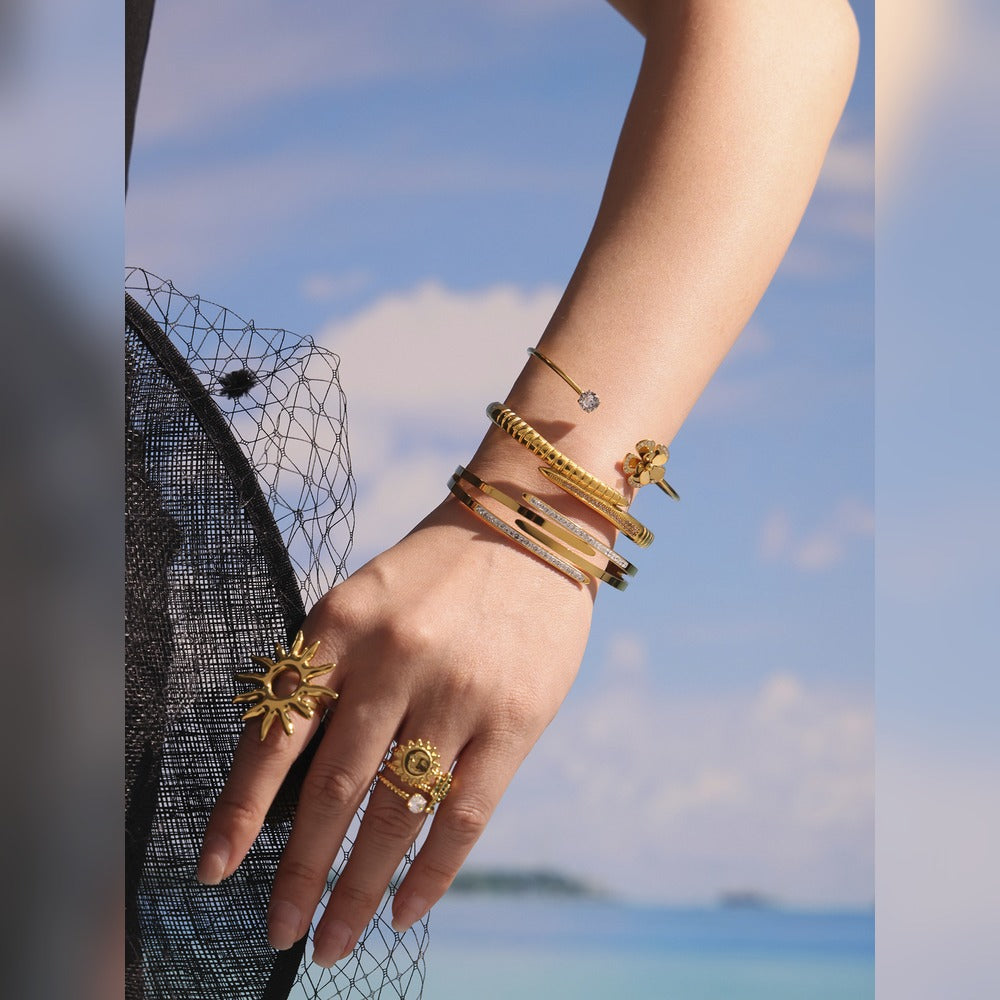 Model wearing stacked gold-tone nail bangles with rings in an outdoor fashion look