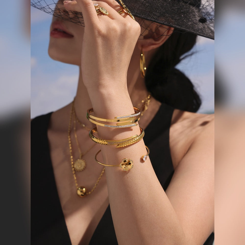 Model wearing a layered gold-tone nail bangle bracelet stack in a close-up outdoor portrait