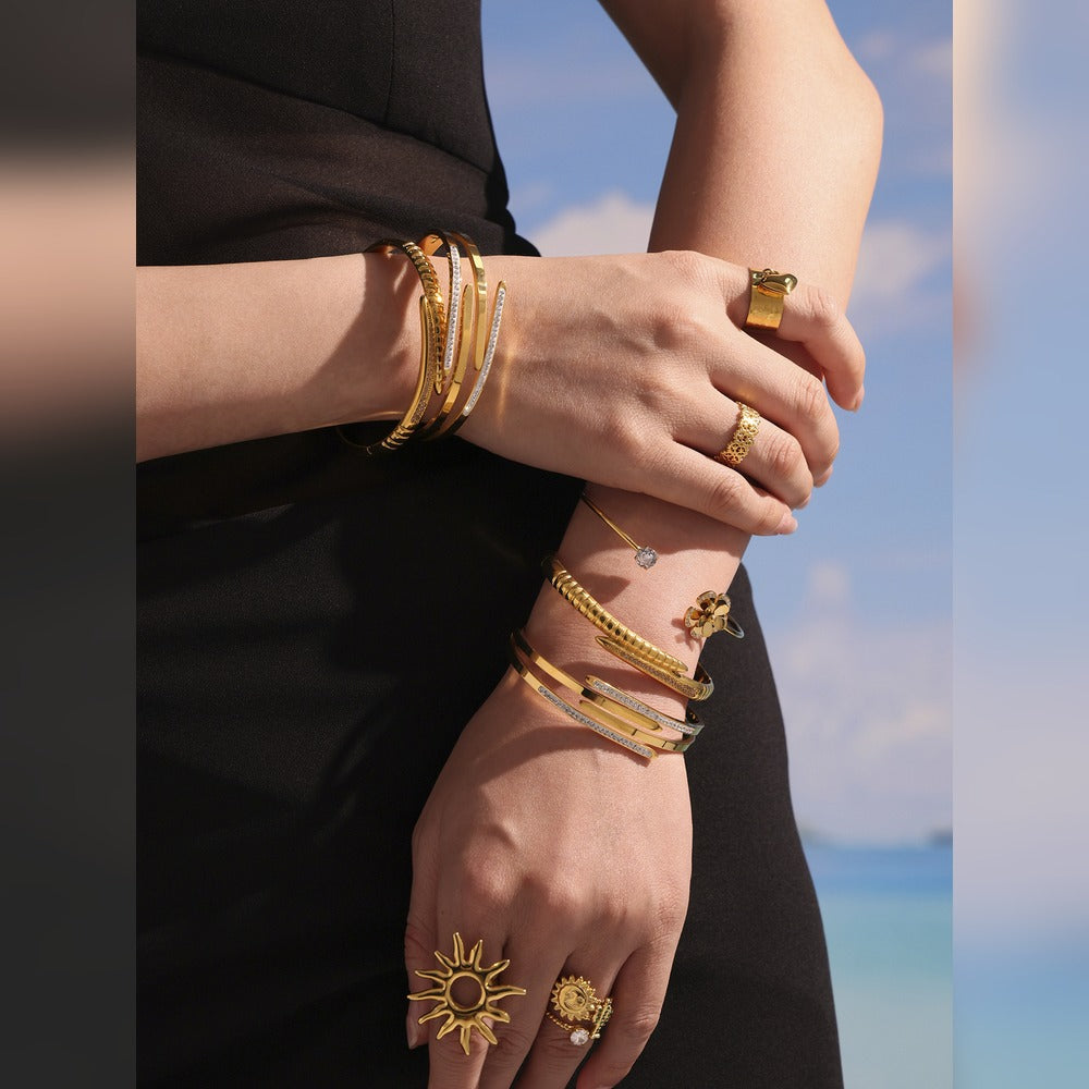 Model styling gold-tone nail bangle bracelets on both wrists with statement rings