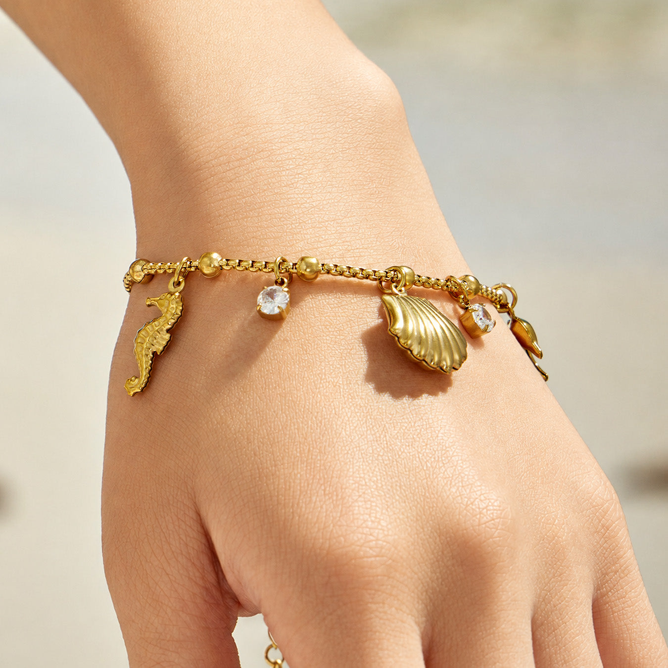 Model wearing a gold ocean charm bracelet with shell and sea-life details