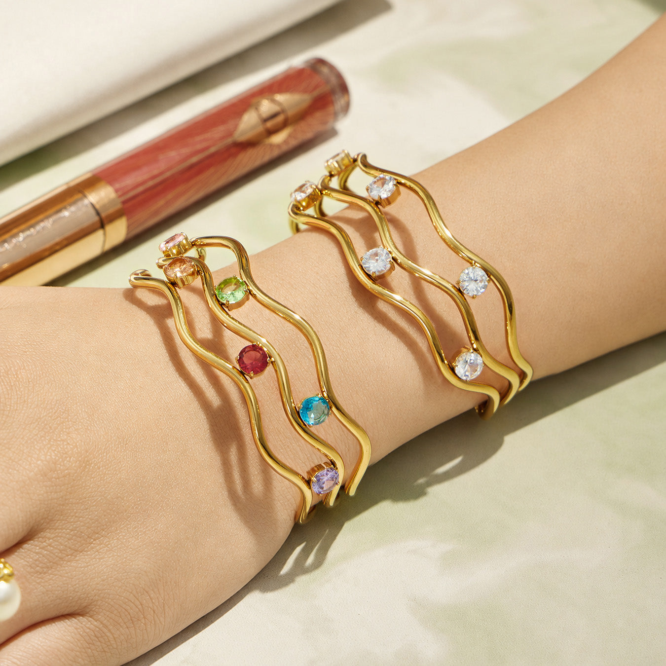 Wrist detail of a gold three-layer open bangle with cubic zirconia
