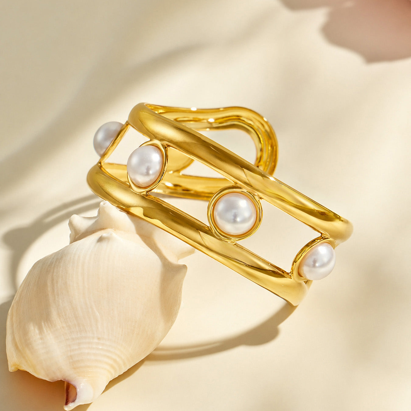 Product view of a gold pearl cage cuff bracelet showing its curved open structure