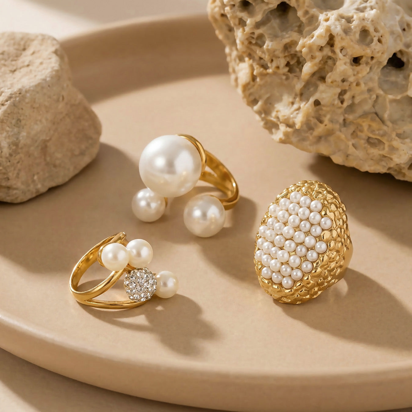 Gold pearl cluster and open-band rings arranged on textured neutral fabric