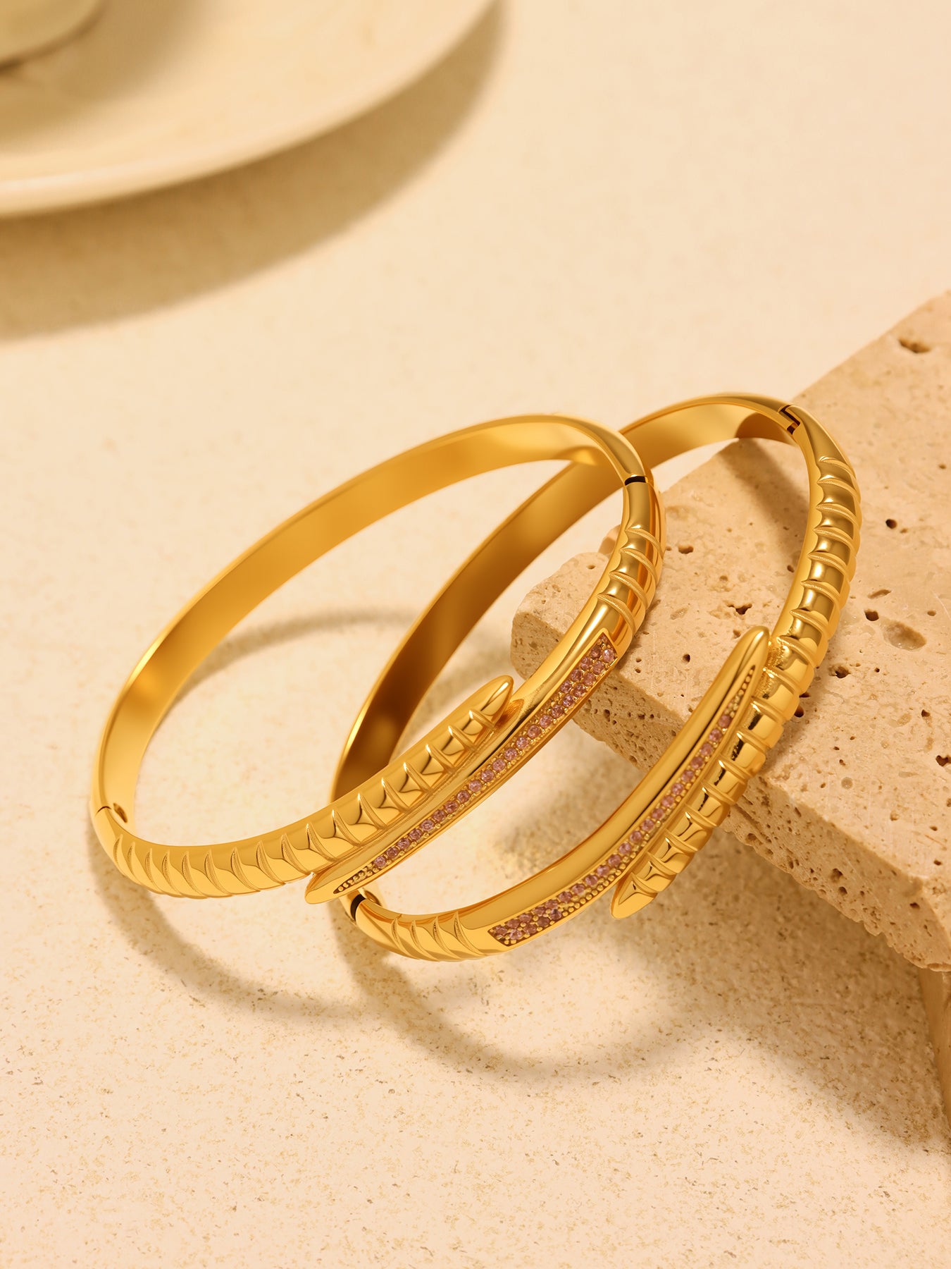 Pair of gold-tone nail bangle bracelets with ribbed detailing and pink zircon accents