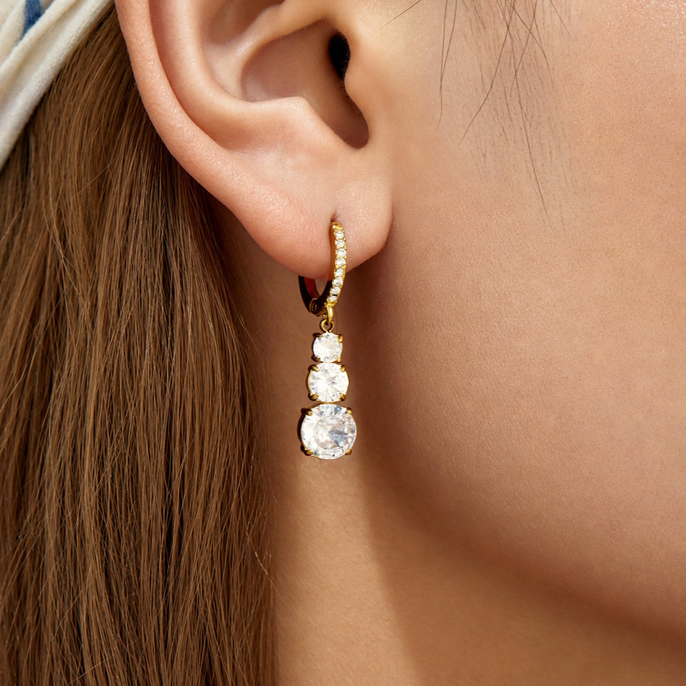 Model wearing a gold drop earring with a clear cubic zirconia droplet