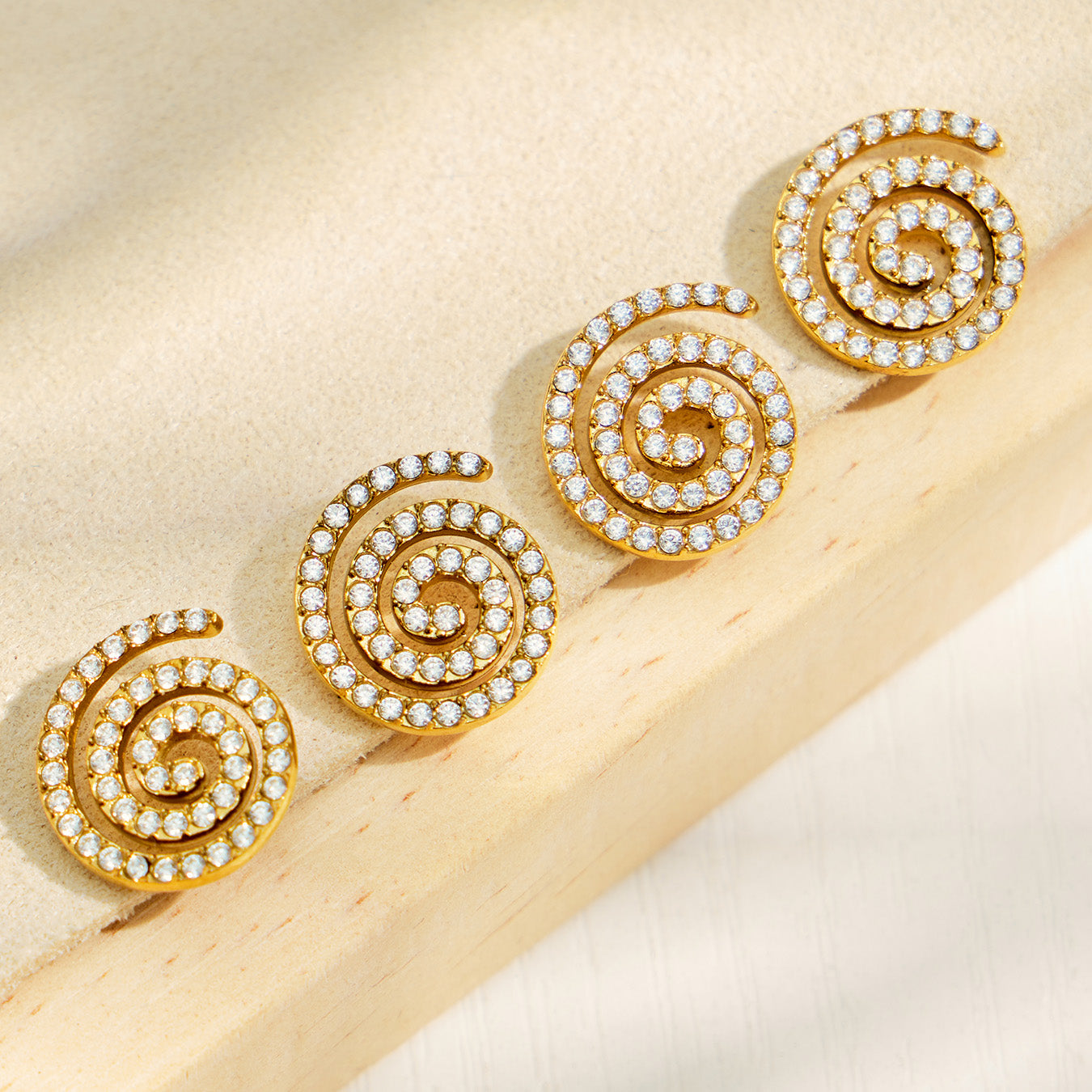 Gold spiral stud earrings displayed on a neutral fabric background