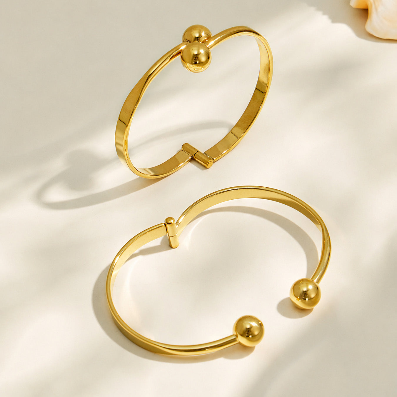 Gold and polished steel double ball cuff bracelets arranged together on a neutral background