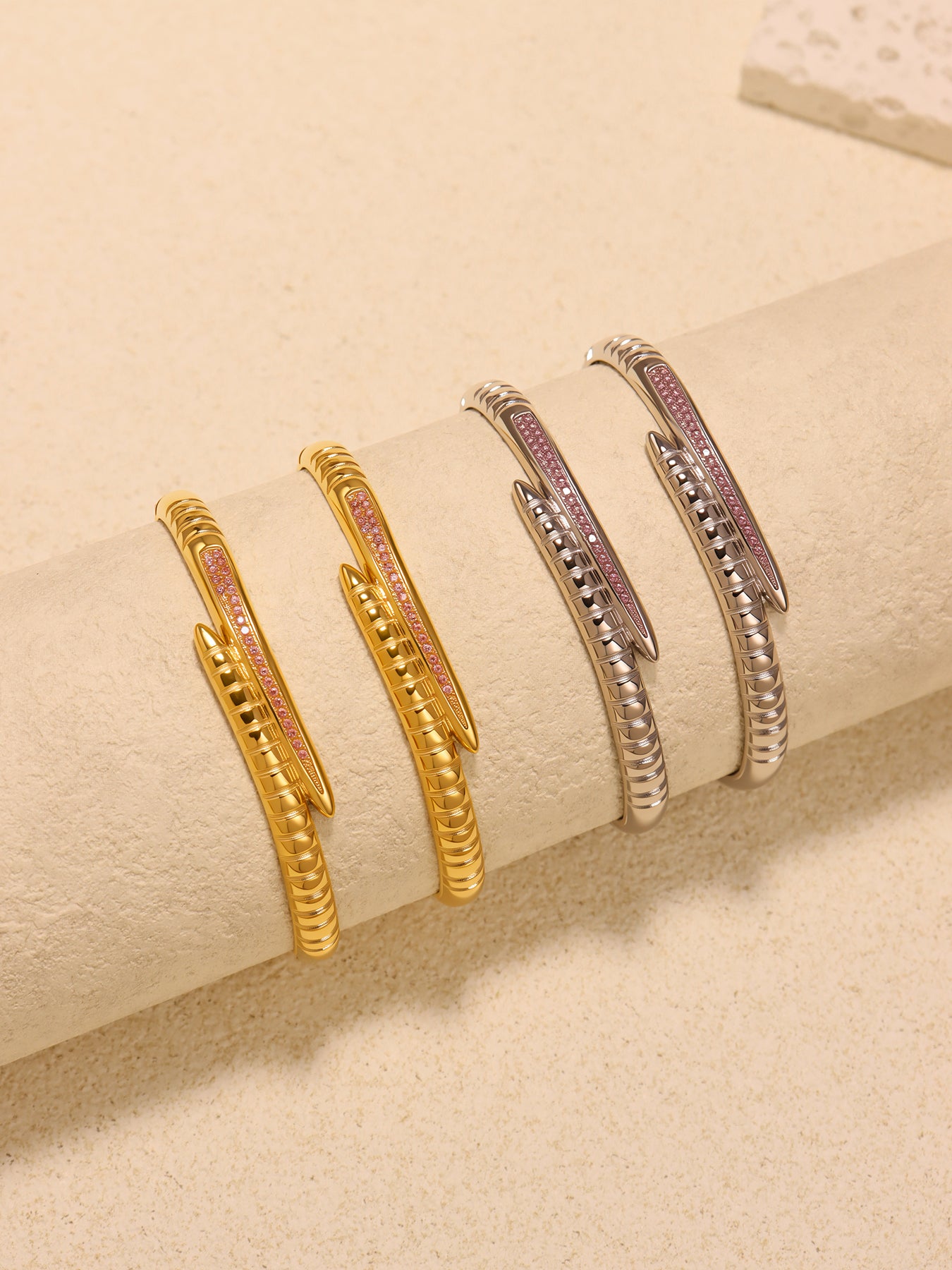 Gold-tone and steel-tone nail bangle bracelets arranged on a cream cylindrical display