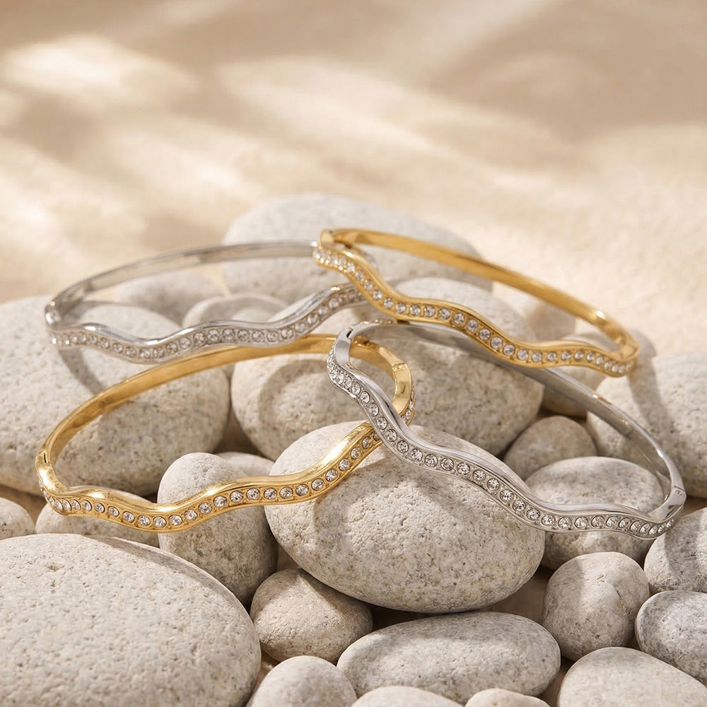 Gold zircon bangle bracelet set on stone display with wavy cuff bracelet, H buckle bangle and round zircon bracelet styles