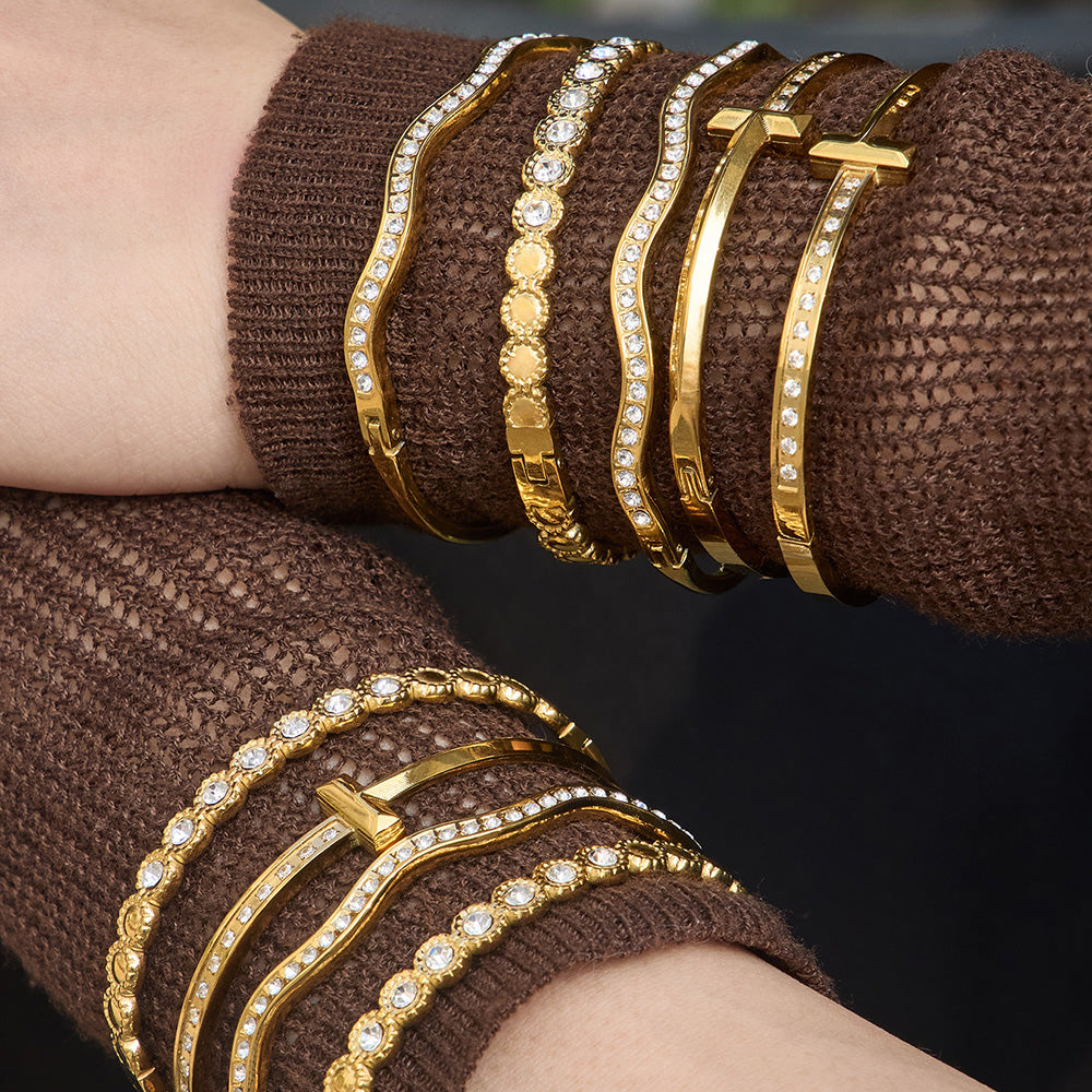 Close up of gold H buckle zircon bangle bracelet stacked with wavy zircon cuff and round zircon bracelet on knit sleeve