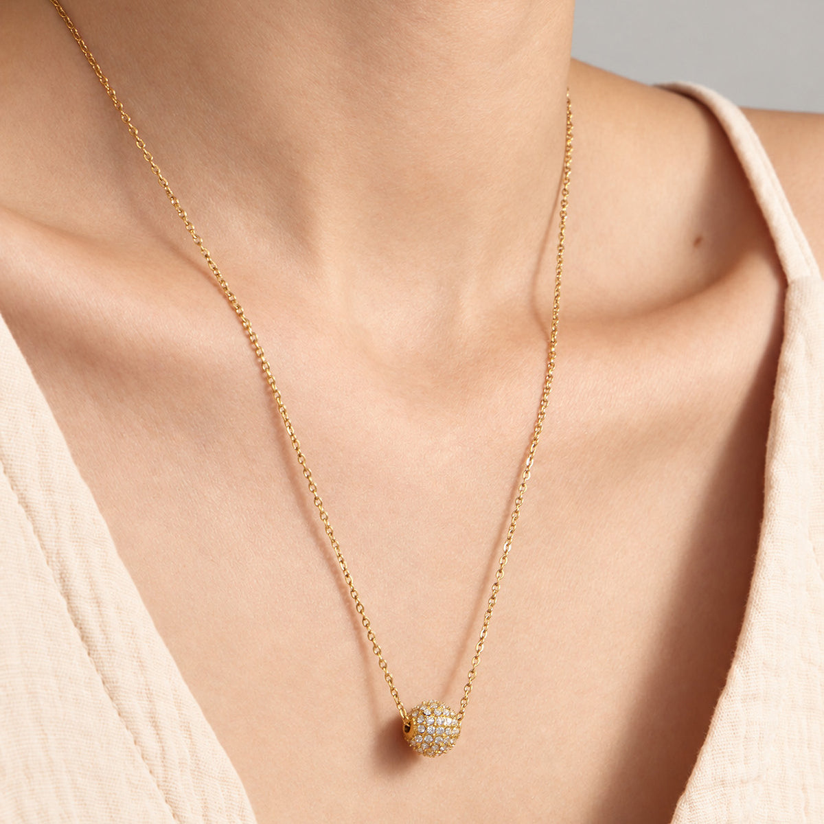 Gold zircon sphere pendant necklace worn at the collarbone