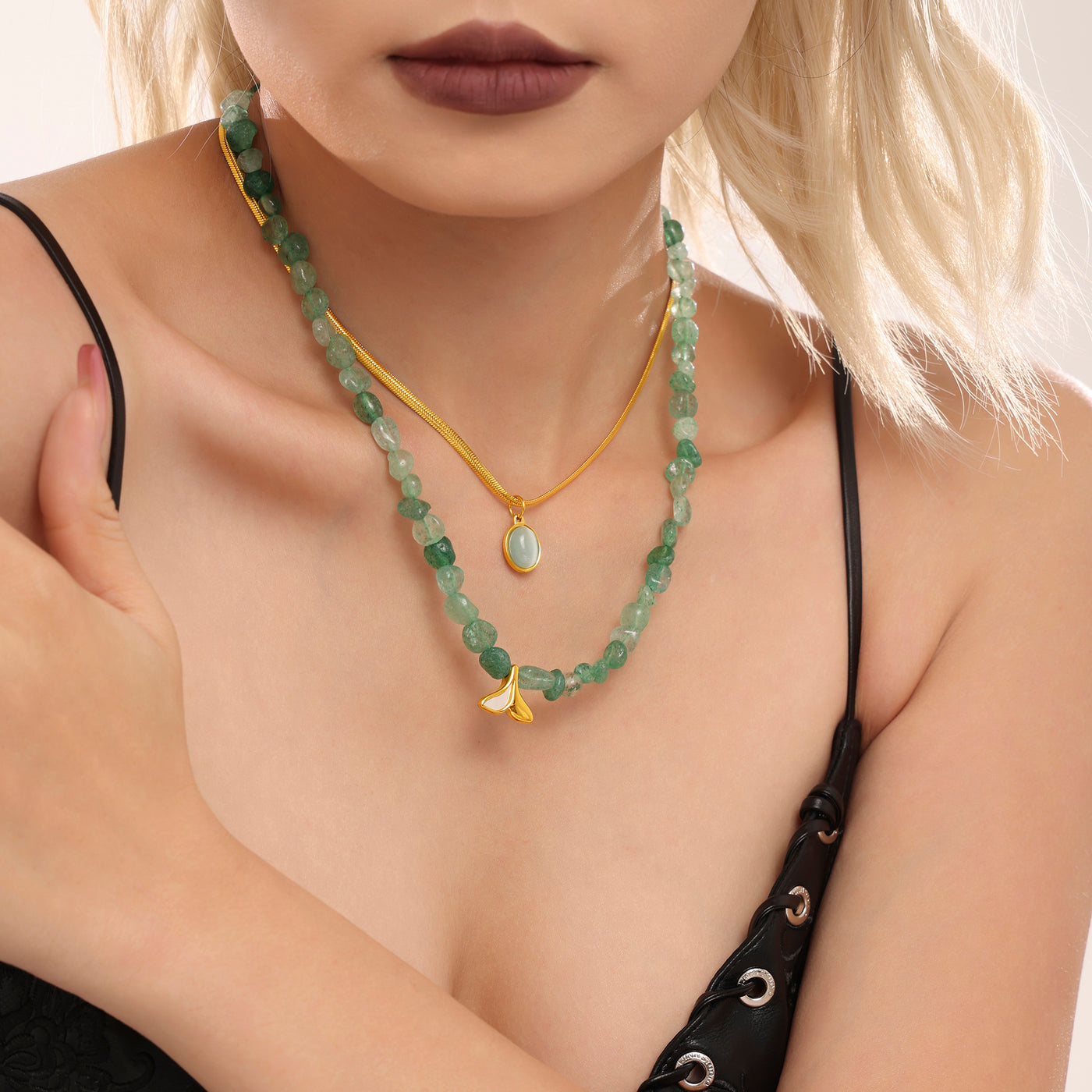 Model wearing a green bead necklace and gold oval pendant chain with a black outfit