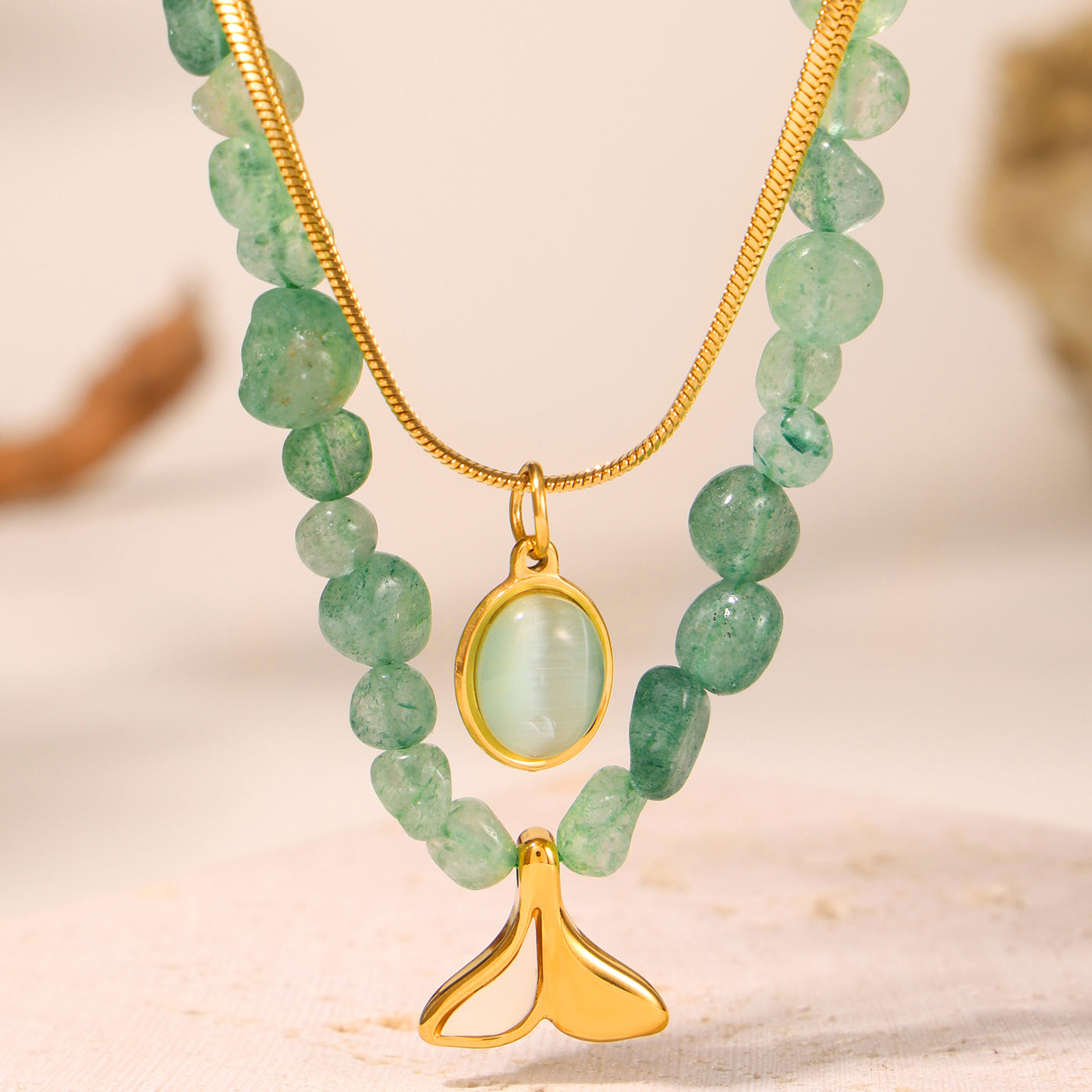 Close-up of green beads, a pale oval pendant and a gold fan-shaped charm