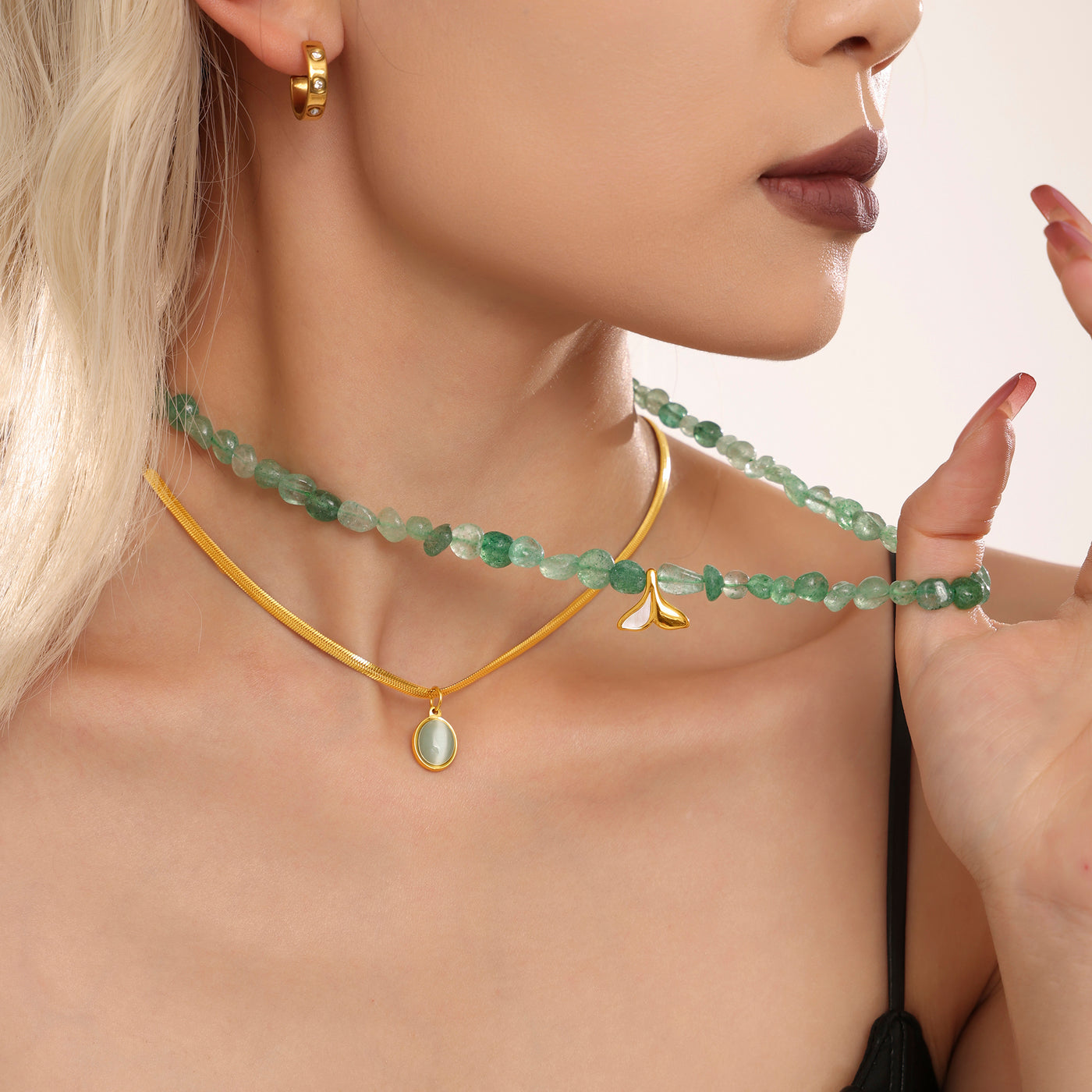 Model adjusting a green beaded necklace layered with a delicate gold chain