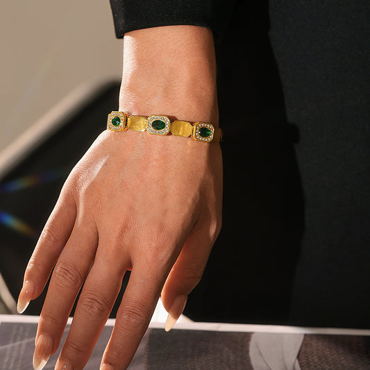 Model wearing a gold green glass clasp bangle with geometric links and polished finish