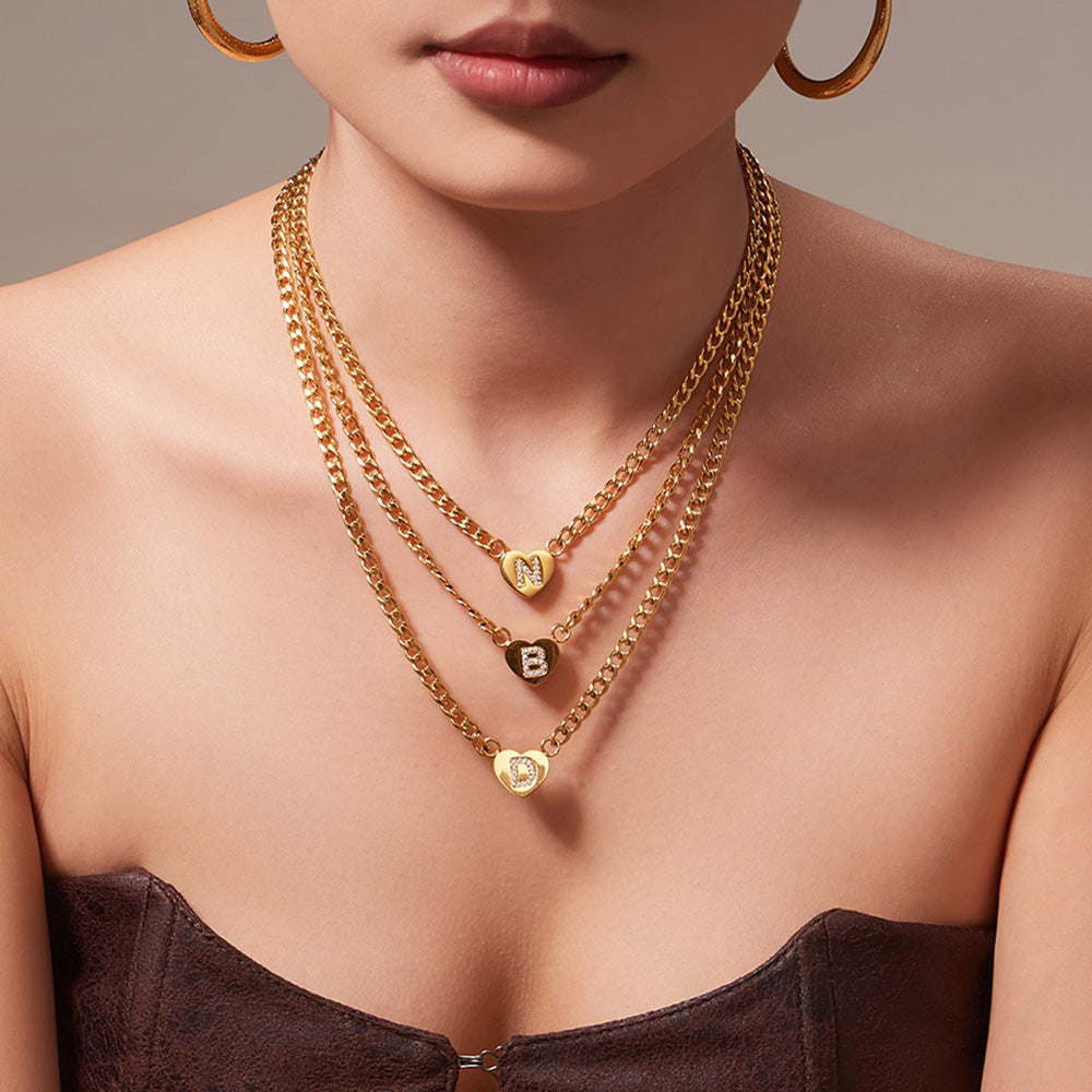 Close-up of a model wearing layered gold-tone zircon initial heart curb chain necklaces
