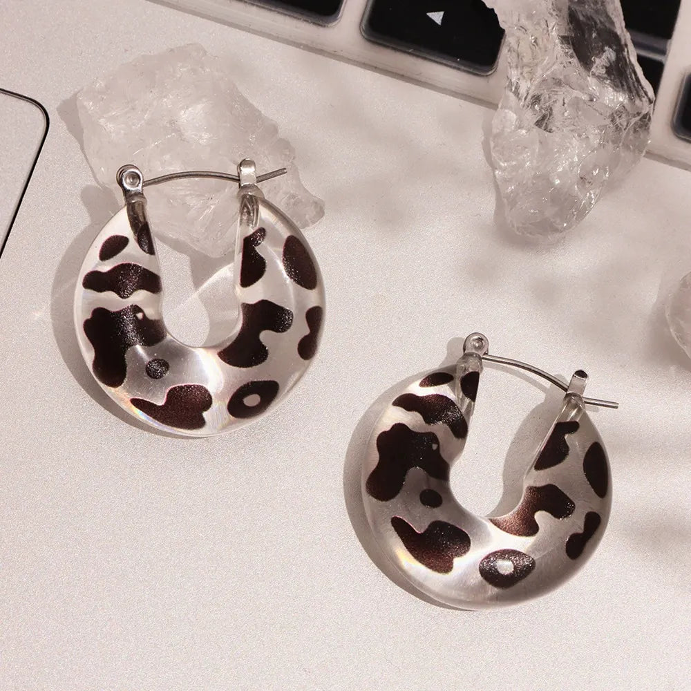 Close-up of black and white spotted resin U-shaped hoop earrings on a neutral background