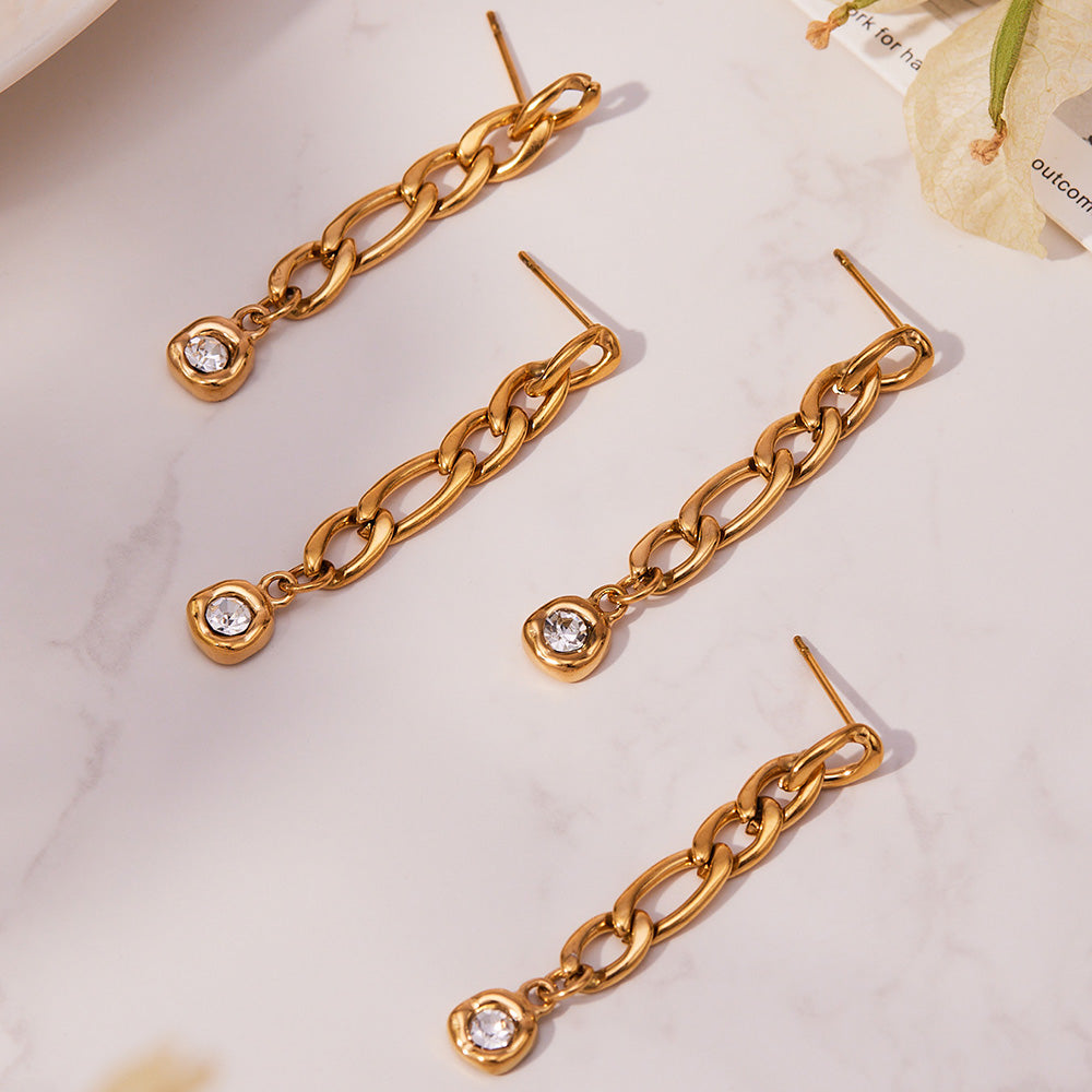 Long gold link chain zircon drop earrings arranged diagonally on a light background