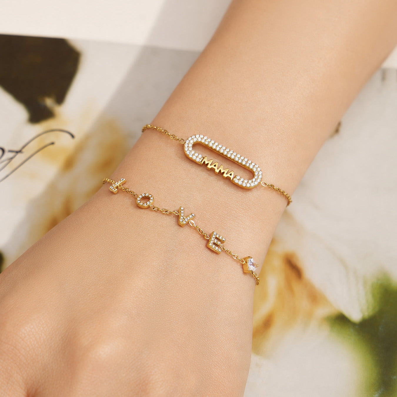 Close-up of layered gold letter bracelets including a MAMA zircon bar design