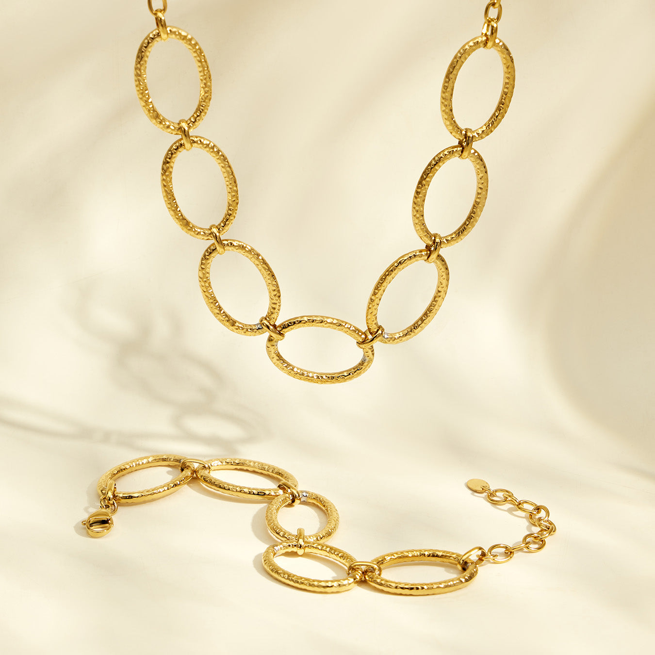 Matching gold oval link necklace and bracelet arranged together on a light background