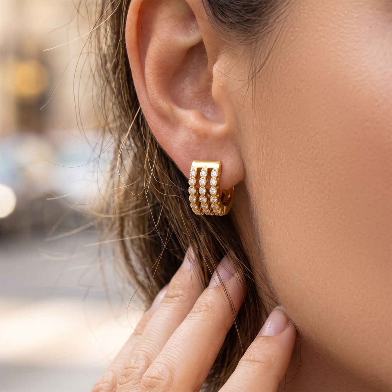 Model touching a small triple-row pavé zircon huggie earring