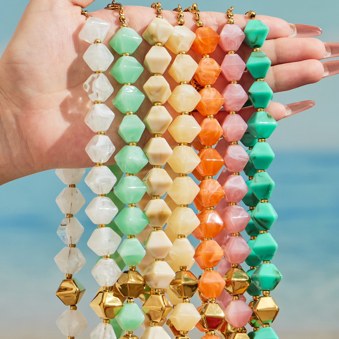 Hand holding multiple colorful faceted resin bead strands showing green pink orange ivory and white options