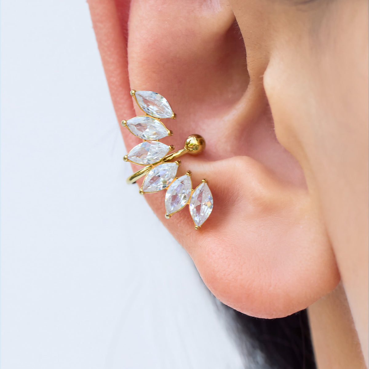 Gold-tone stainless steel leaf ear cuff worn on the ear, featuring clear marquise-shaped stones arranged in a curved pattern