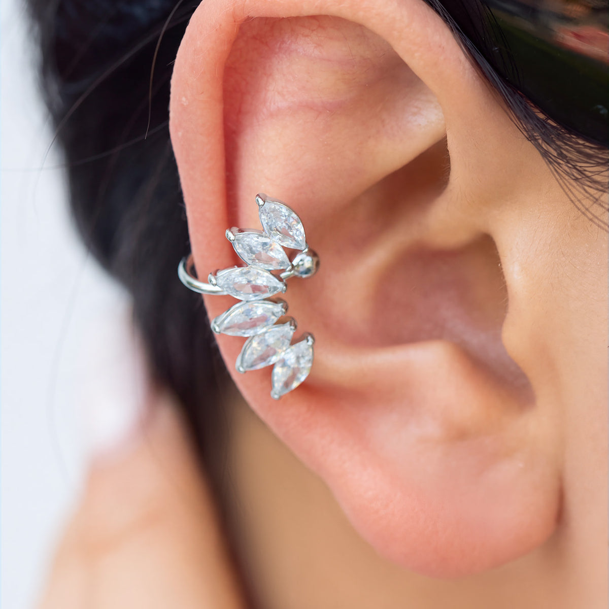 Model wearing a silver leaf-shaped ear cuff with sparkling clear stones following the curve of the outer ear