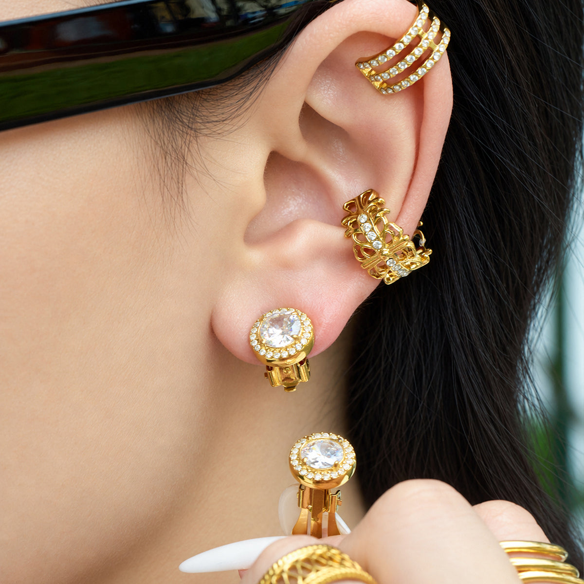 Model wearing a round gold halo clip-on earring while holding a matching clip-on accessory near the ear