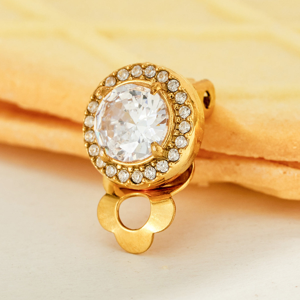 Front view of a gold round halo clip-on earring with a large clear stone encircled by smaller sparkling stones