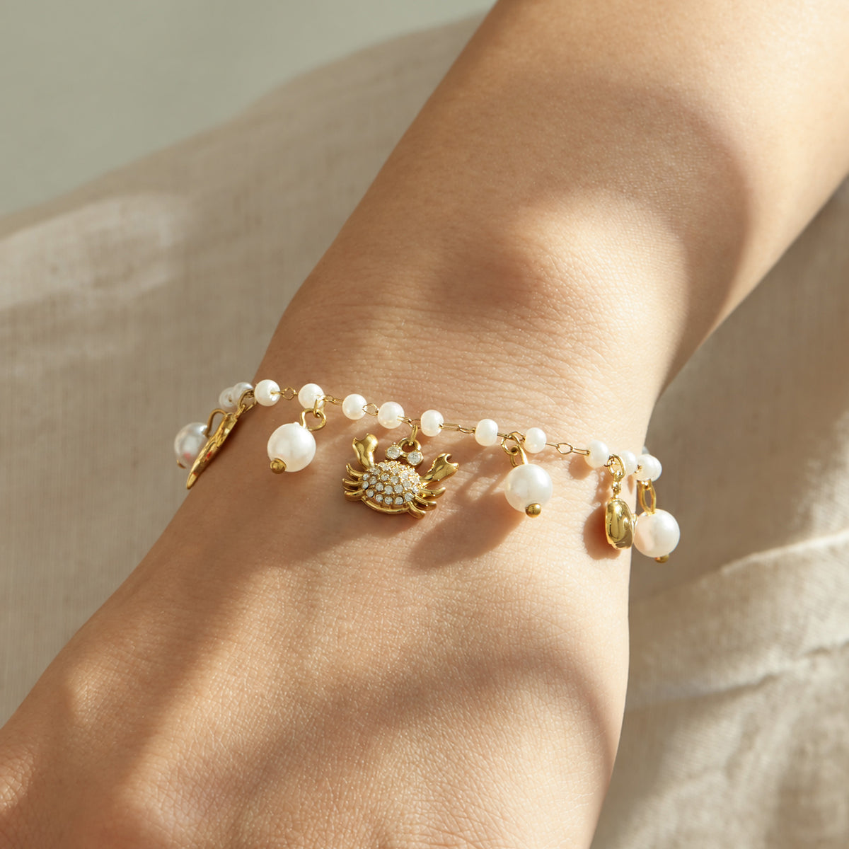 Gold stainless steel ocean charm bracelet with pearl beads shown in a close-up wrist view