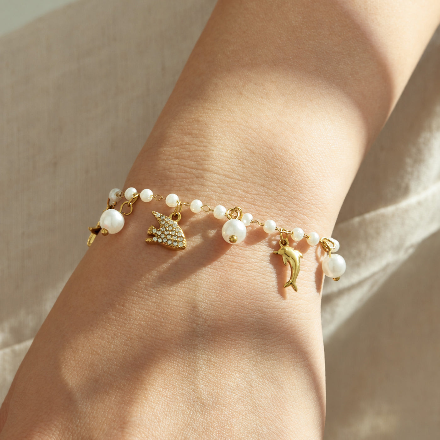 Gold pearl marine charm bracelet with ocean animal details worn on a model wrist