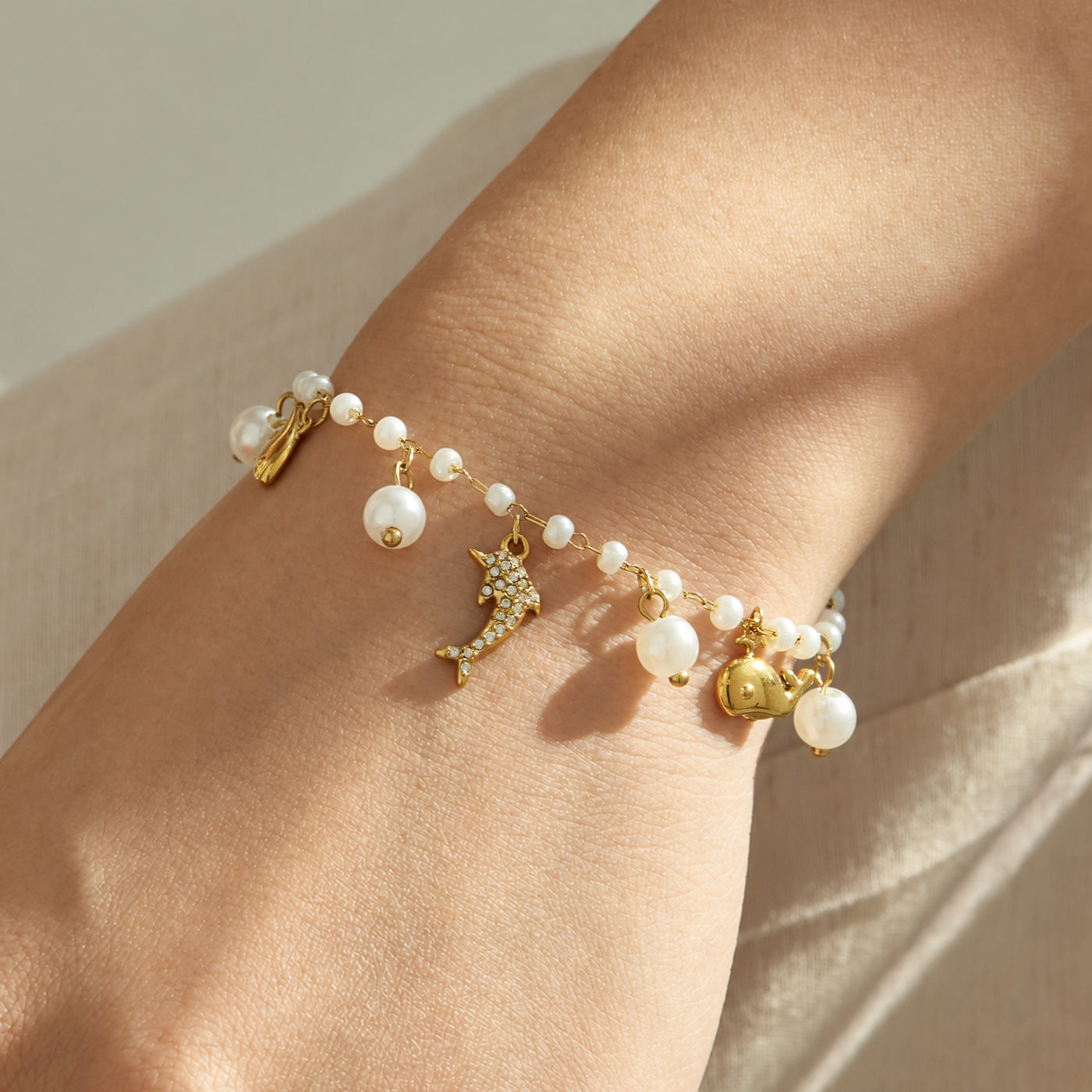 Gold ocean charm pearl bracelet with dangling marine charms and pearl beads worn on the wrist