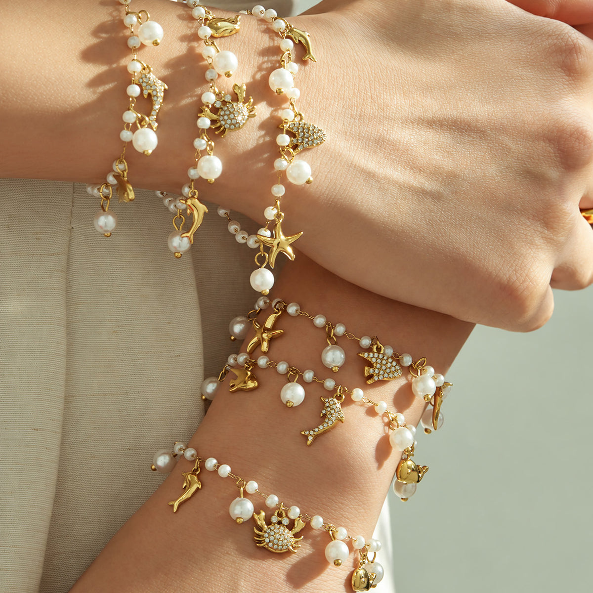 Layered gold ocean charm pearl bracelets worn on a model wrist with marine charms and pearl beads