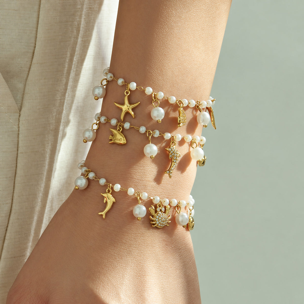 Gold ocean pearl charm bracelets layered on the wrist with sparkling marine-inspired details