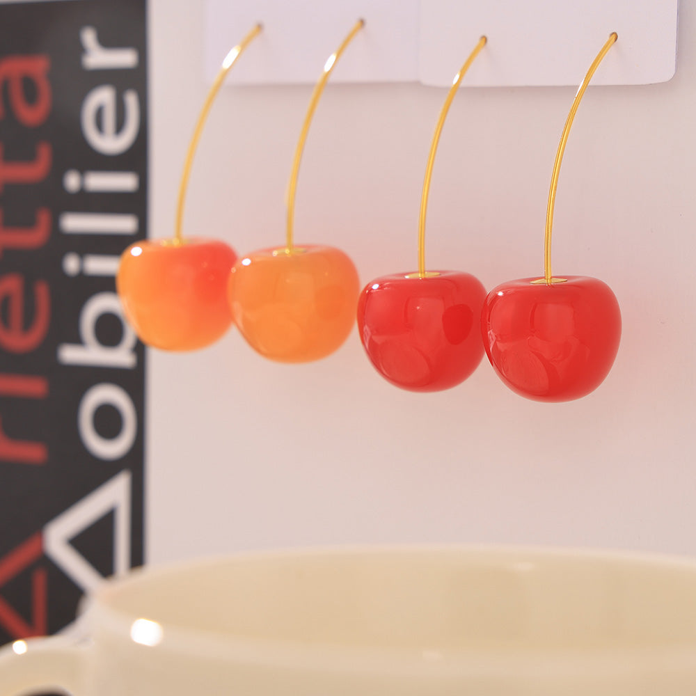 Orange-red and bright red cherry earrings hanging on a clear display stand
