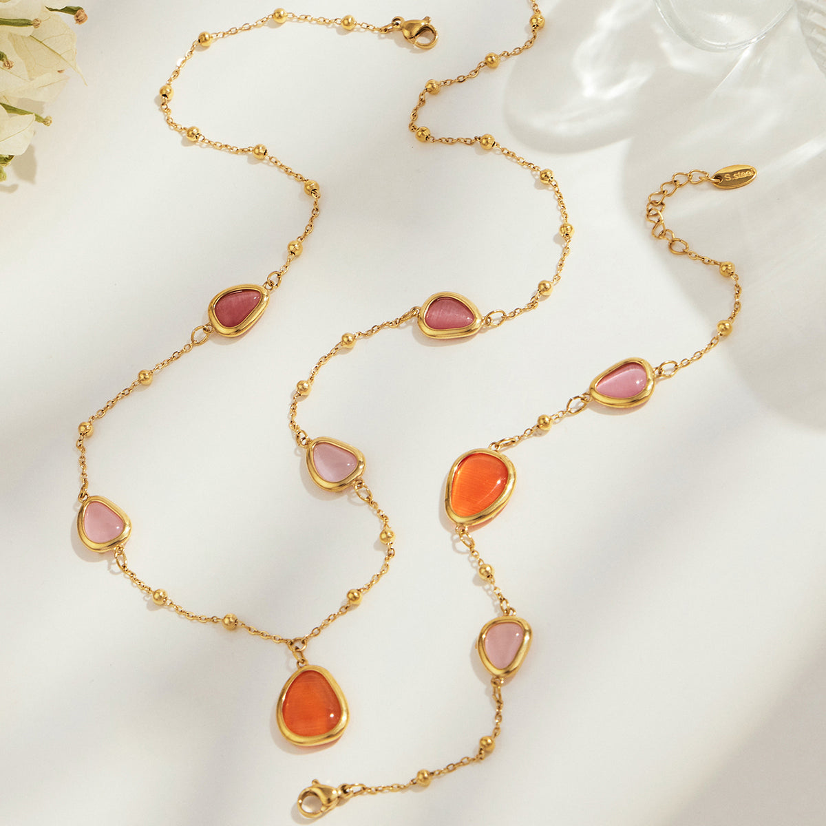 Gold-tone necklace with orange cat eye stone accents arranged in a flat lay