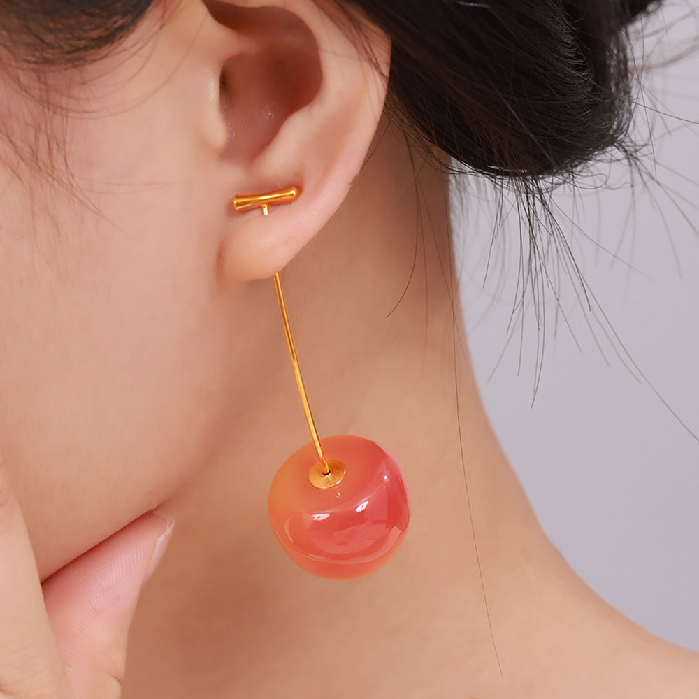 Orange-red cherry drop earrings with long gold-tone stems worn by a model