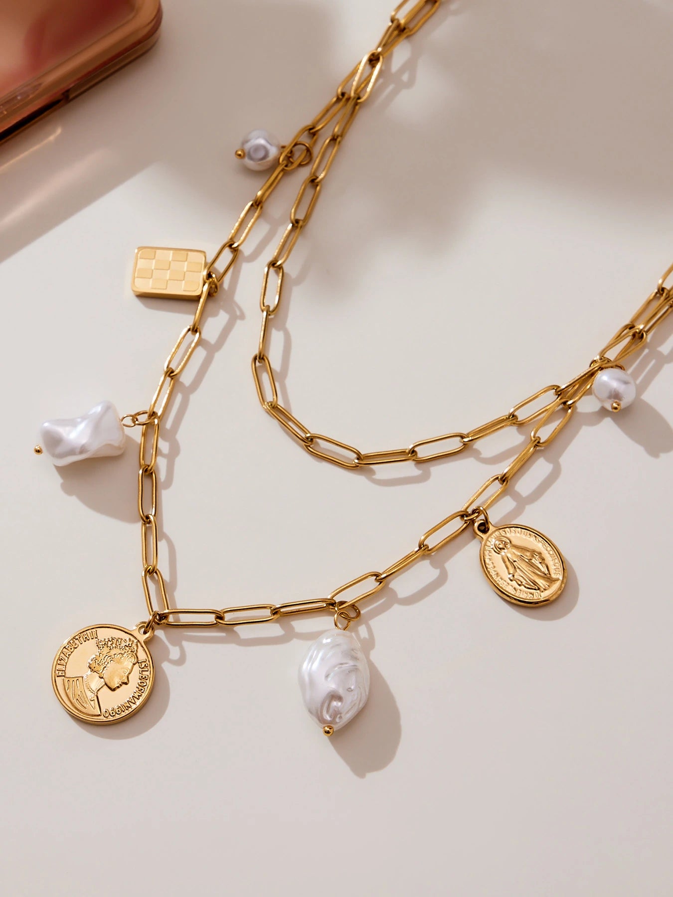 Close-up of paperclip charm necklaces with coin, checkerboard and pearl-look charms