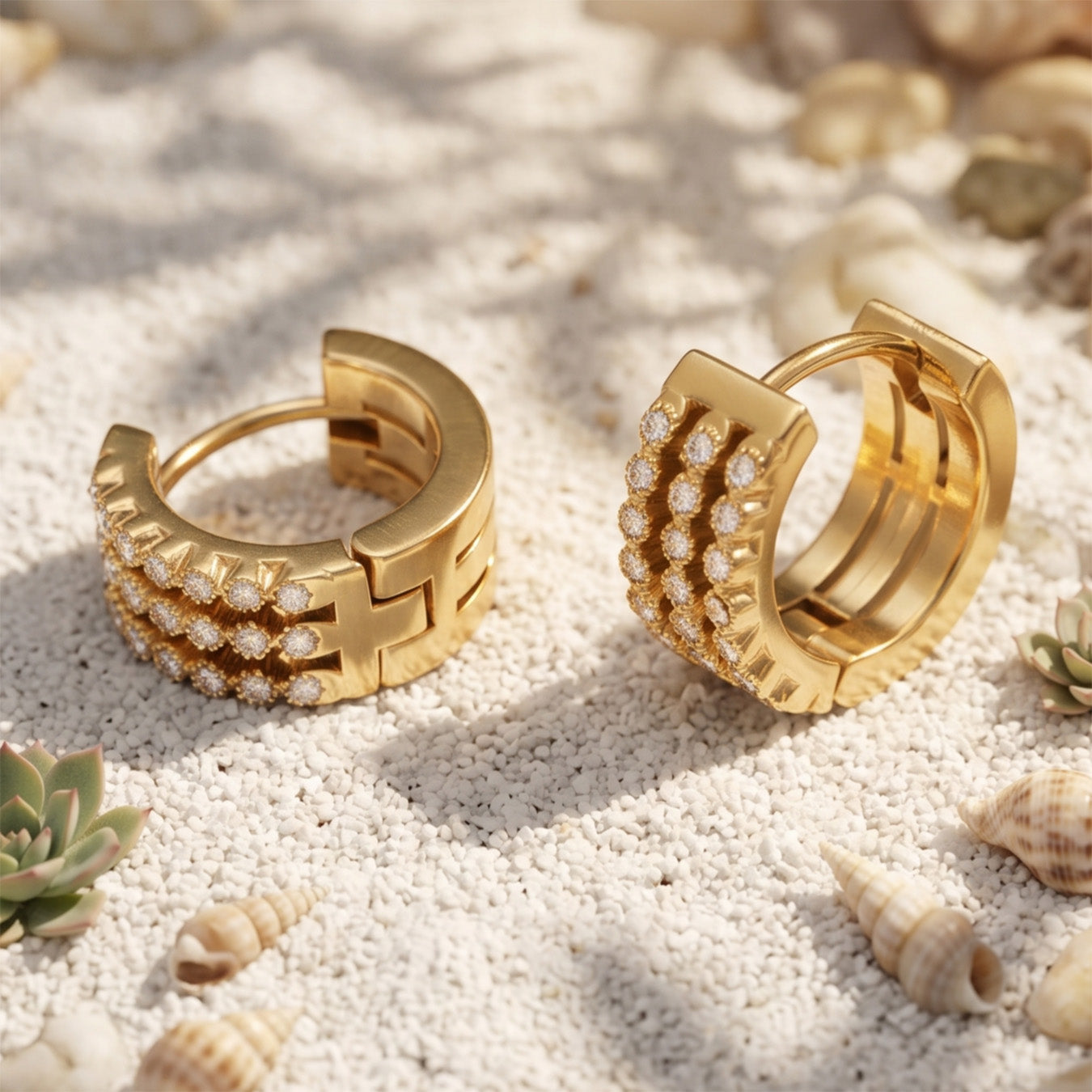 Gold pavé zircon huggie earrings arranged on a softly textured neutral surface